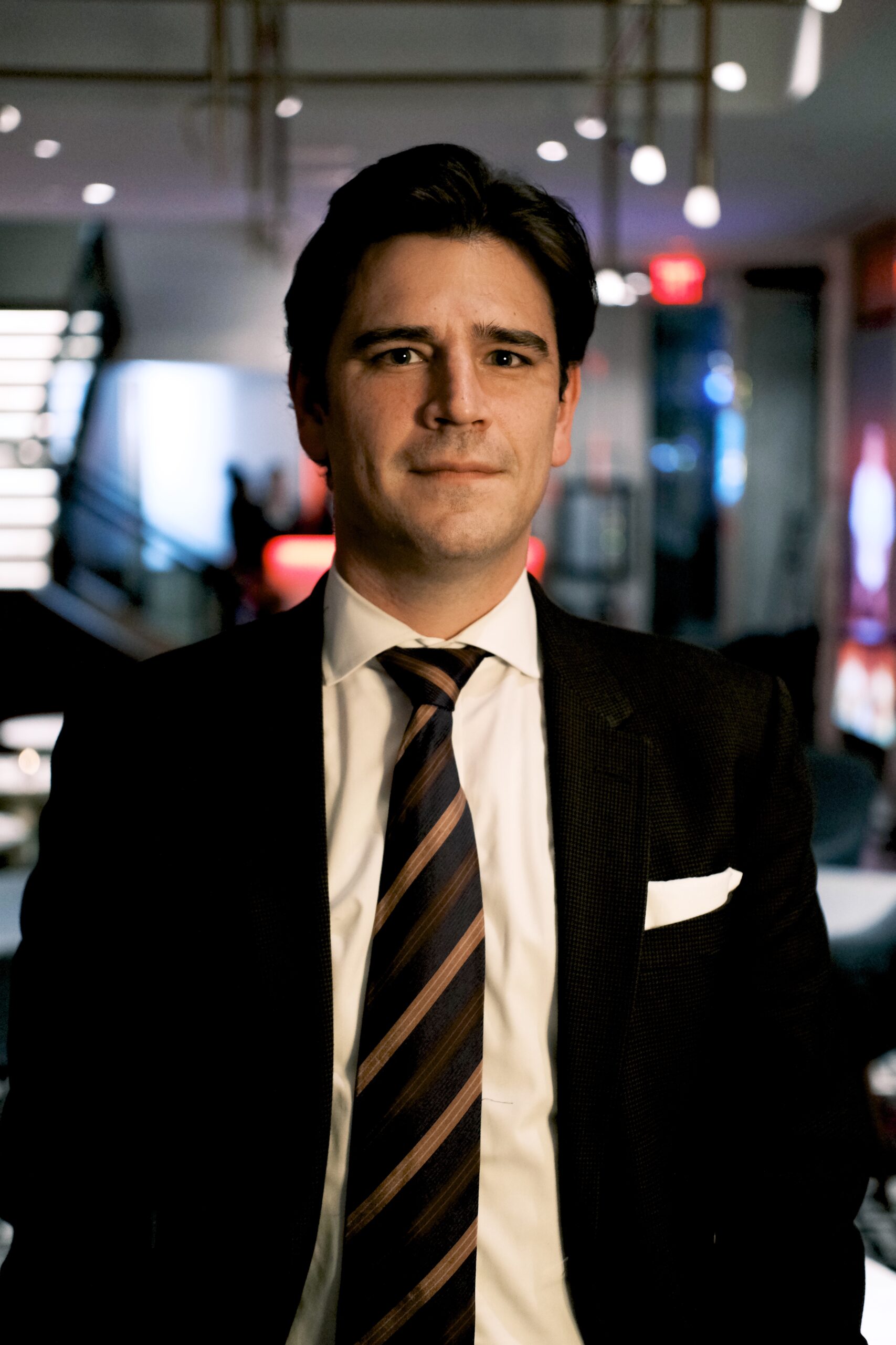 Headshot of Bill McMorris standing in a suit with lights in the background.